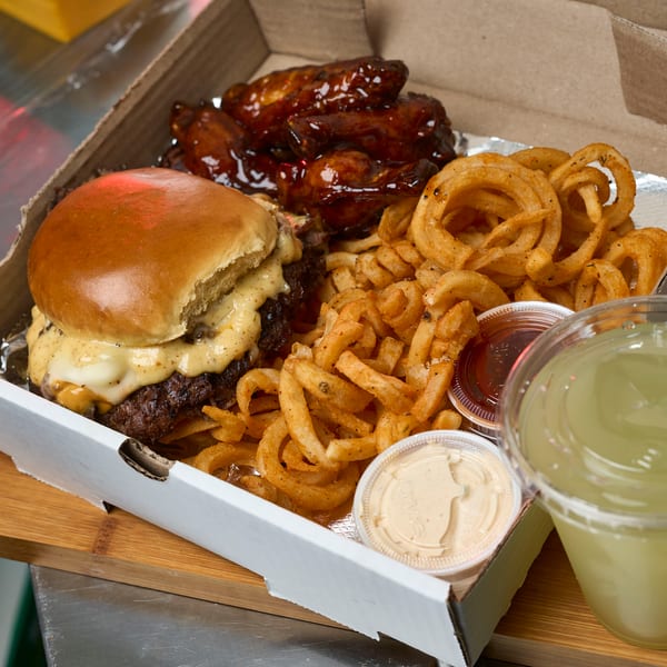 Combo box with smash burger, glazed wings, curly fries, dipping sauces, and lemonade.